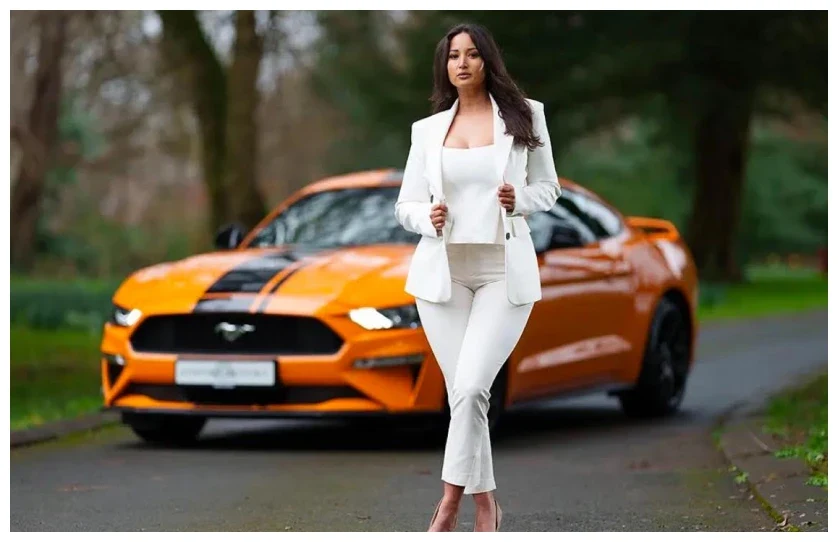 Nadia Adan in a white suit beside an orange Ford Mustang